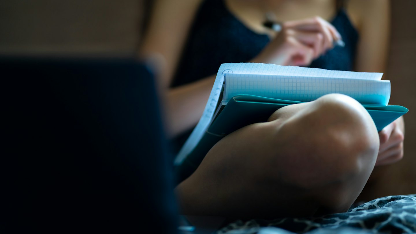 Person taking notes in a spiral notebook with a pen.