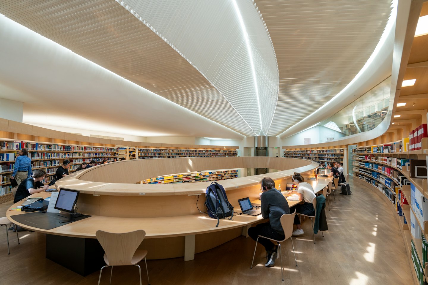 Students studying at a modern library's curved wooden desk.